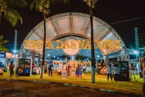 Barracas coloridas da 14ª Festa das Nações em Rondonópolis, com público desfrutando de gastronomia e cultura em apoio à Comunidade Divina Providência.