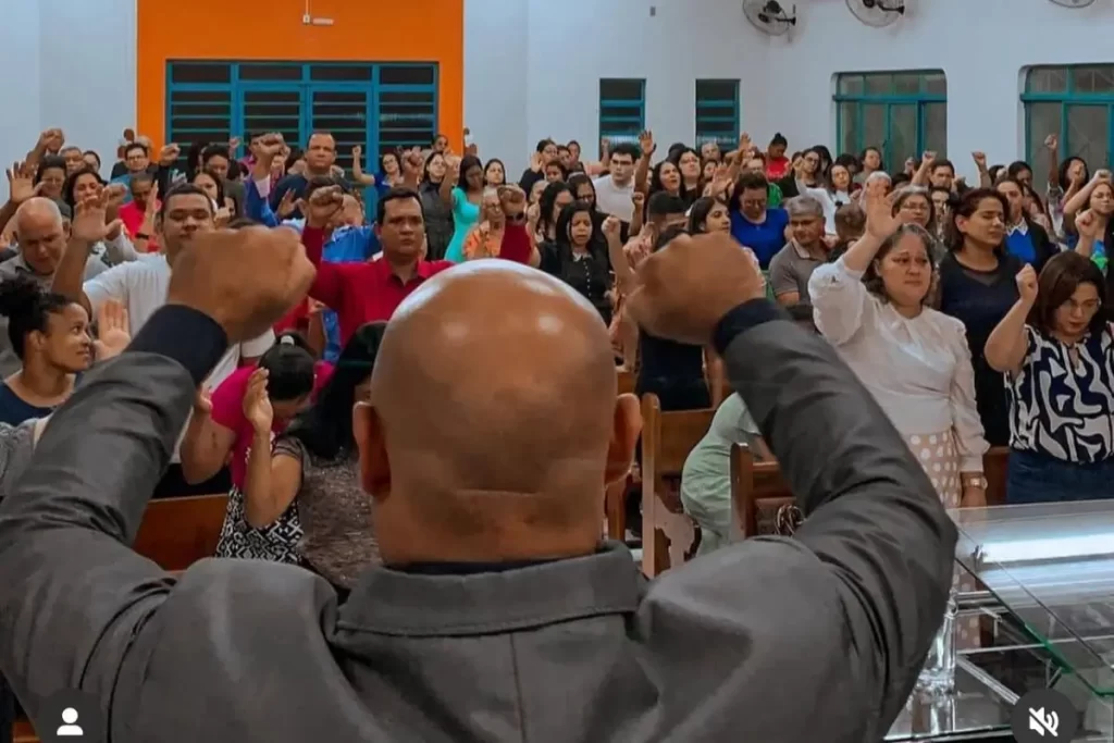 A Jornada de Fé e Serviço do Pastor Sidnei Alexandre em Rondonópolis 4 Pastor Sidnei Alexandre conduzindo um momento de louvor com fiéis levantando as mãos em adoração na Assembleia de Deus em Rondonópolis.