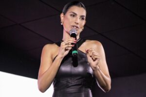 Cíntia Chagas sorri em palco lotado segurando microfone durante palestra de comunicação