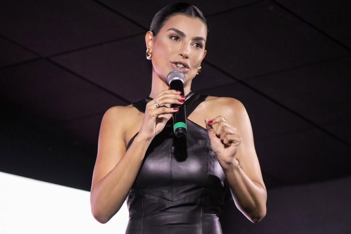 Cíntia Chagas sorri em palco lotado segurando microfone durante palestra de comunicação