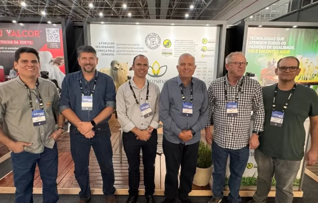 Dirigentes da Aprosmat e da Unipasto no estande do Acricorte 2025 em Cuiabá; Gutemberg Carvalho Silveira e Pierre Patriat lideram representantes na maior feira de pecuária de corte do Brasil, banner de sementes de pastagem ao fundo