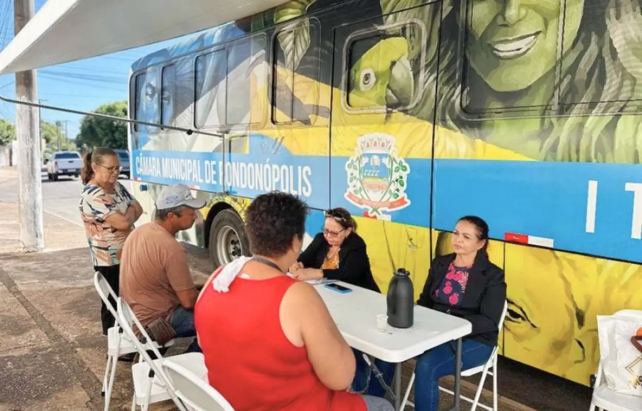 ônibus da Câmara Municipal estacionado na praça do São Francisco com mesa, cadeiras e moradores assinando abaixo‑assinado