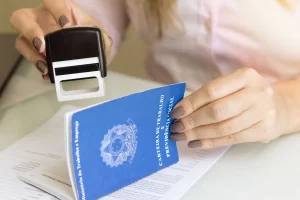 profissional de RH carimbando carteira de trabalho com documentos de férias sobre a mesa