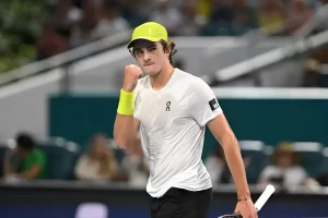 João Fonseca ergue os braços em celebração após vitória em Wimbledon, com placa do placar ao fundo