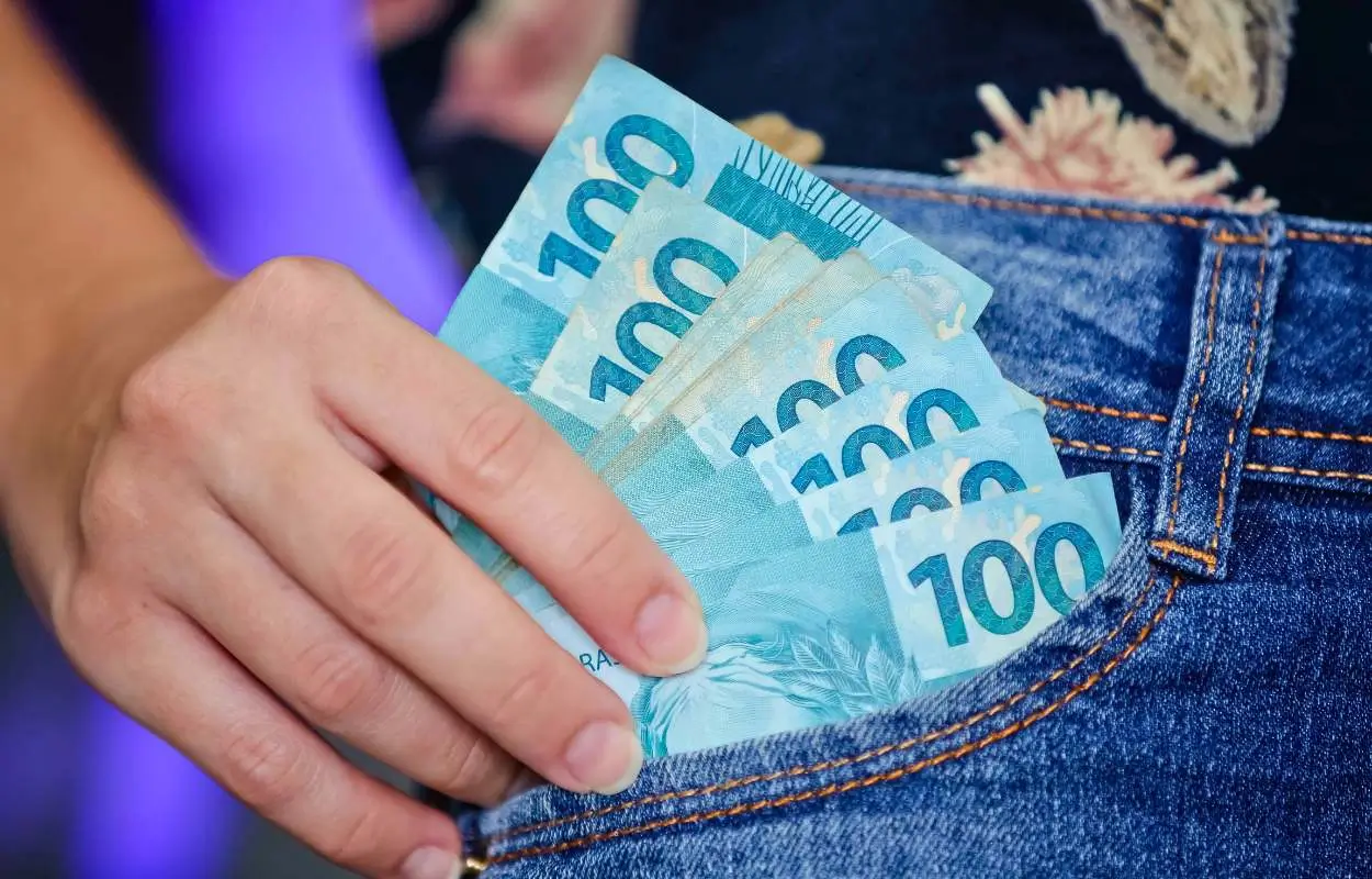 trabalhadora segura notas de dinheiro após receber o PIS da Caixa